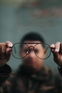 man holding black framed glasses in the forefront with the man and background blurred Tag: 2020 reflection gratitude grief